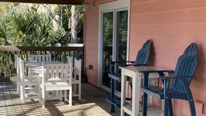 En træterrasse med et bord og stole, et overdækket område og udsigt til grønne omgivelser.