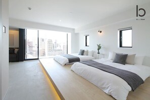 Una habitación de hotel moderna con dos camas, un ventanal amplio que ofrece vistas a la ciudad y un diseño minimalista.