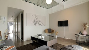 Ein modernes Wohnzimmer mit einem Glastisch, einer Couch, einem Fernseher und einem Bild an der Wand.