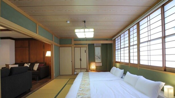 A traditional Japanese-style room with tatami flooring, a large bed with white bedding, a sofa, and sliding doors. - b hotel Kaniwasou | Miyajima Island Stay 31 (Hiroshima City)