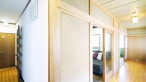 A hallway with wooden flooring, a sliding door, and a visible bed with pillows in the adjacent room. - b hotel Kaniwasou | Miyajima Island Stay 31 (Hiroshima City)