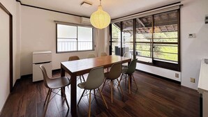 A dining area with a wooden table and chairs, large windows, and a ceiling light fixture. - b hotel Kaniwasou | Miyajima Island Stay 31 (Hiroshima City)