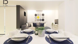 Une chambre d’hôtel moderne avec un coin repas aménagé pour quatre personnes, un canapé, une télévision et une œuvre d’art murale.