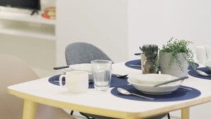 Un coin repas moderne et minimaliste, avec une table blanche, des sets de table bleus et une petite plante en pot. Un verre d’eau et une tasse blanche sont posés sur la table.