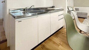 Una cocina moderna con muebles blancos, un lavamanos de acero inoxidable y una campana extractora integrada.