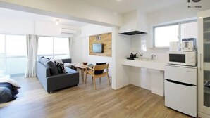 Una habitación de hotel moderna con kitchenette, sofá, comedor y un amplio ventanal.