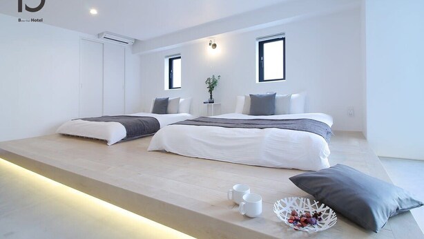 A modern hotel room with two beds, a small table, and a plant.