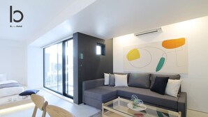 A modern living room with a grey sofa, a glass coffee table, and a large window offering a city view.