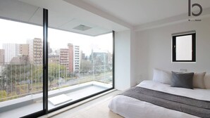 A modern hotel room with a large balcony, a bed with white bedding, and a city view. - b hotel 601 Premium City View Apartment (Hiroshima City)
