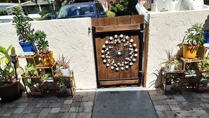 Une porte en bois ornée de motifs métalliques décoratifs, flanquée de part et d’autre de plantes en pot.