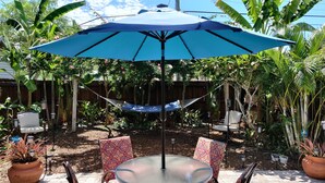 Une terrasse extérieure avec une table ronde, des chaises et un parasol bleu.