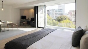 Een moderne hotelkamer met een groot bed, een bureau met stoel, een televisie en een balkon met uitzicht op de stad.