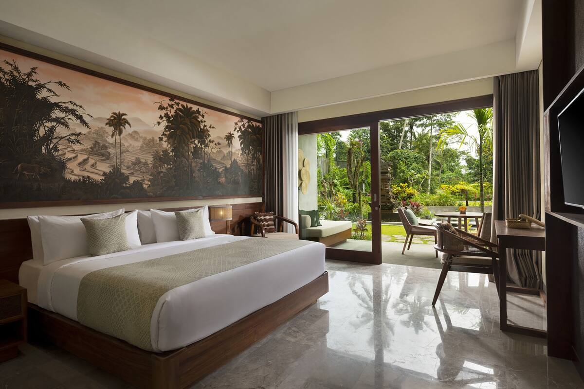 A spacious bedroom with a large bed, a dining area, and a view of lush greenery.