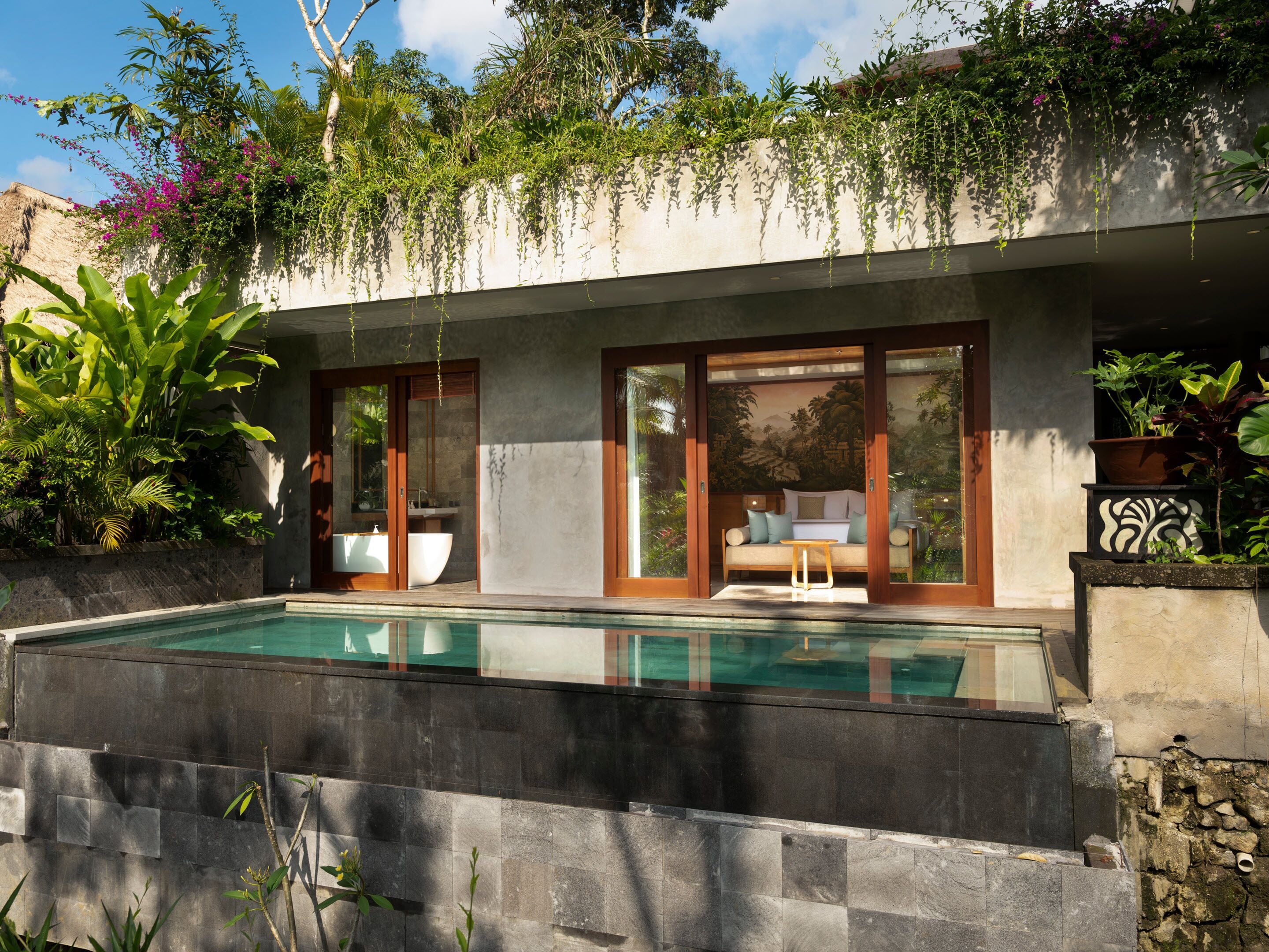 A modern outdoor pool area with a glass-enclosed seating area and lush tropical plants.