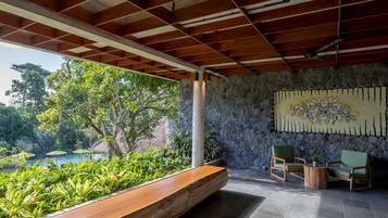 A covered outdoor seating area with a wooden bench, two chairs, and a small table. A stone wall with a floral mural is visible in the background.