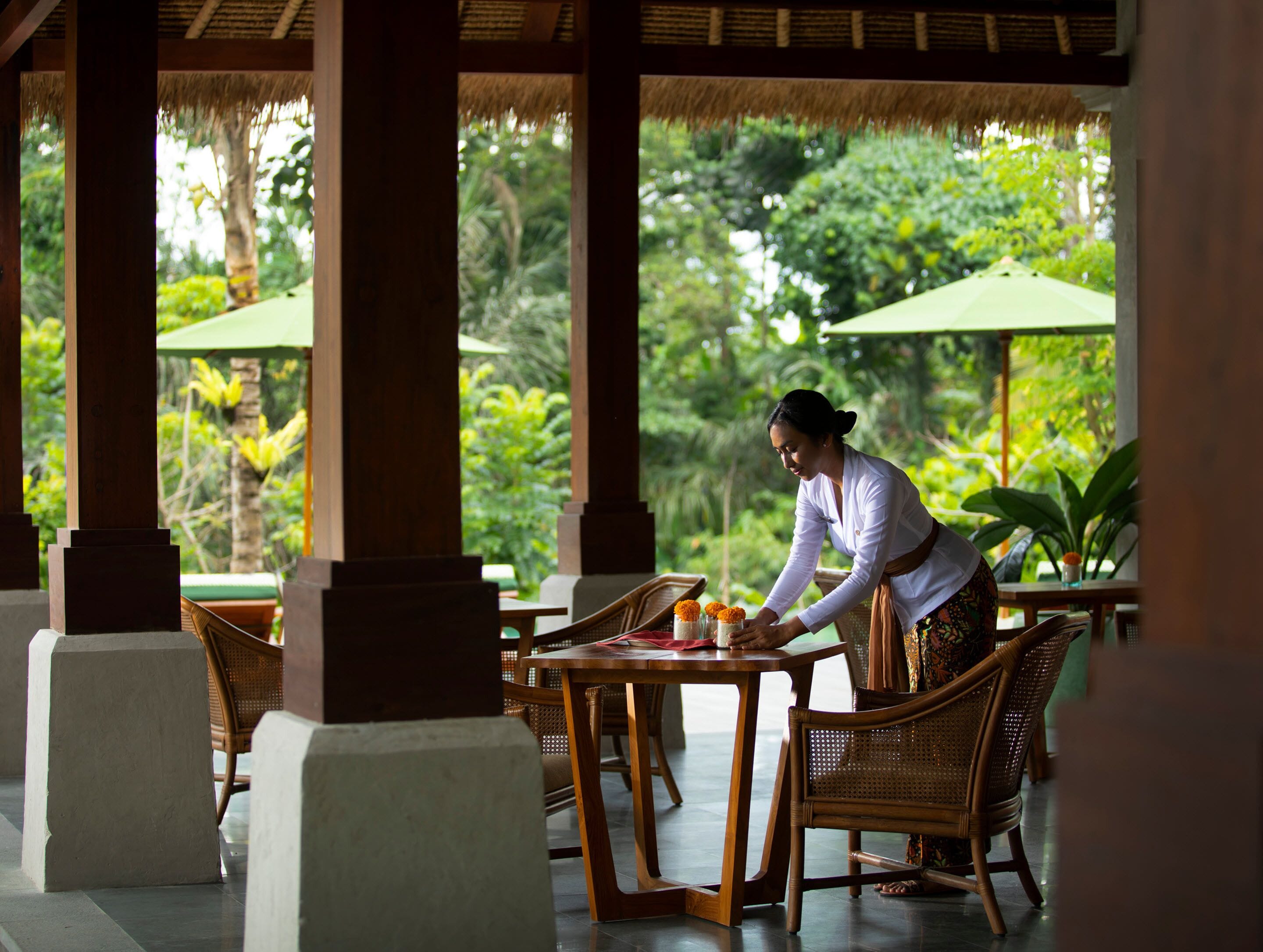 A covered outdoor dining area with wooden furniture and thatched roof pillars.