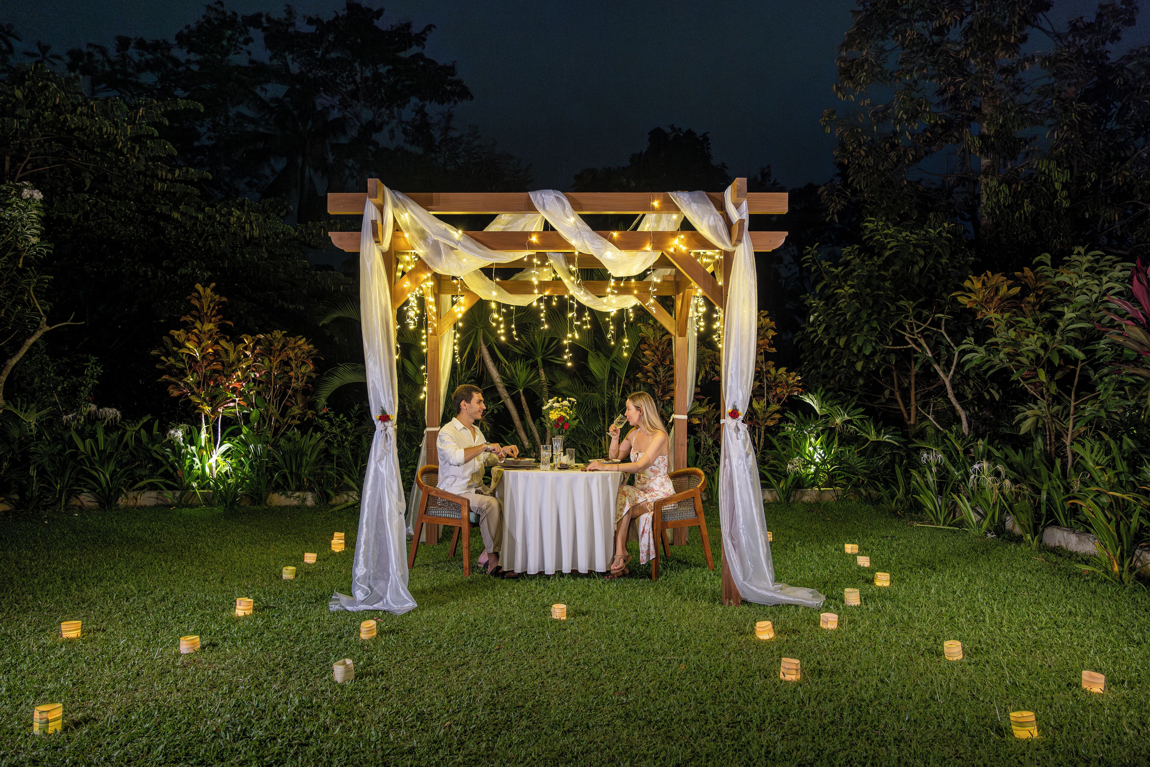 A gazebo with a table and chairs, surrounded by greenery and string lights.