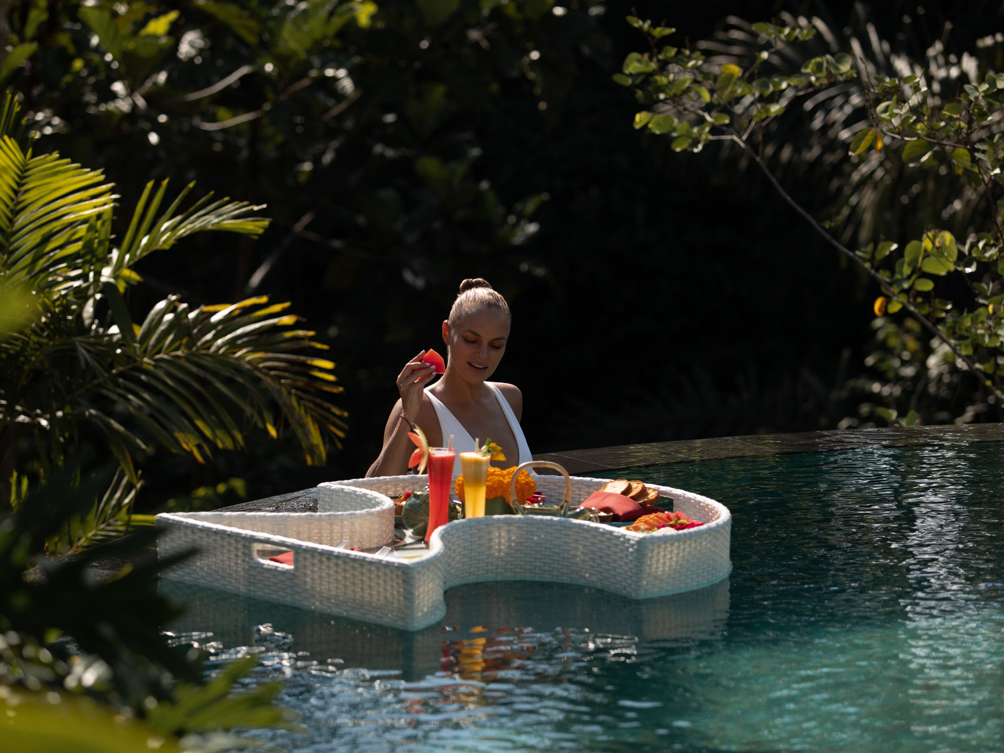A person on a floating platform in a pool surrounded by greenery.