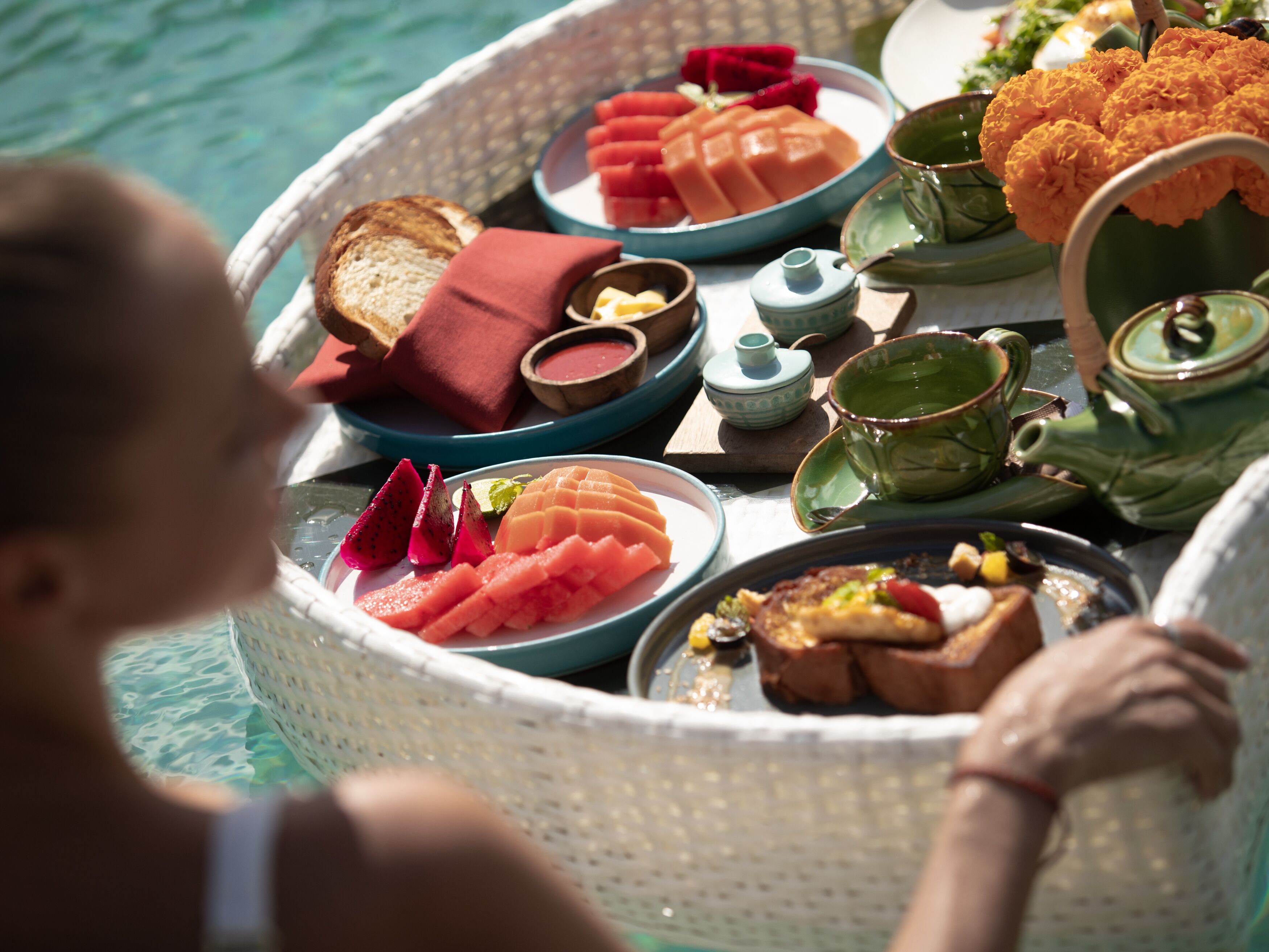 A breakfast setup with various food items and tea sets on a table by a pool.