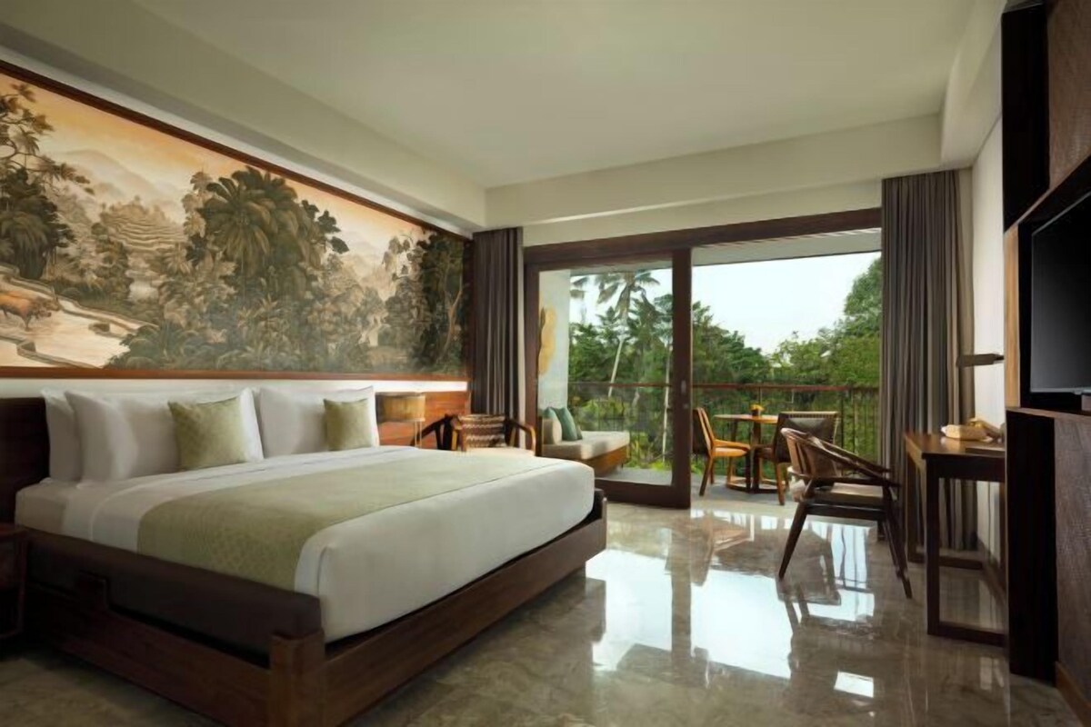 A bedroom with a large bed, a painting on the wall, a balcony with a table and chairs, and a TV.