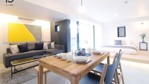 A modern hotel room with a dining area, a sofa, a bed, and a large window. - b hotel 401 Premium City View Apartment (Hiroshima City)