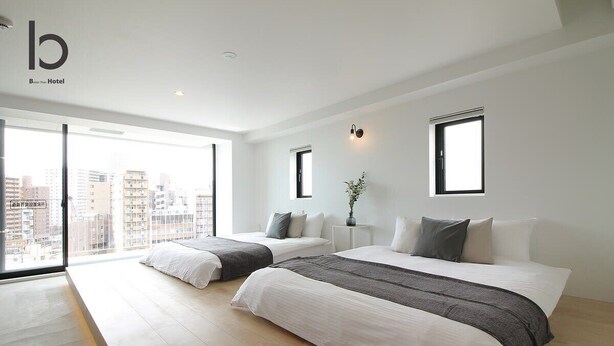 Quarto de hotel moderno com duas camas, janelas amplas e vista para a cidade.