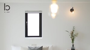 Quarto de hotel com uma cama, janela, luminária fixada na parede e uma pequena mesa com um vaso de flores.