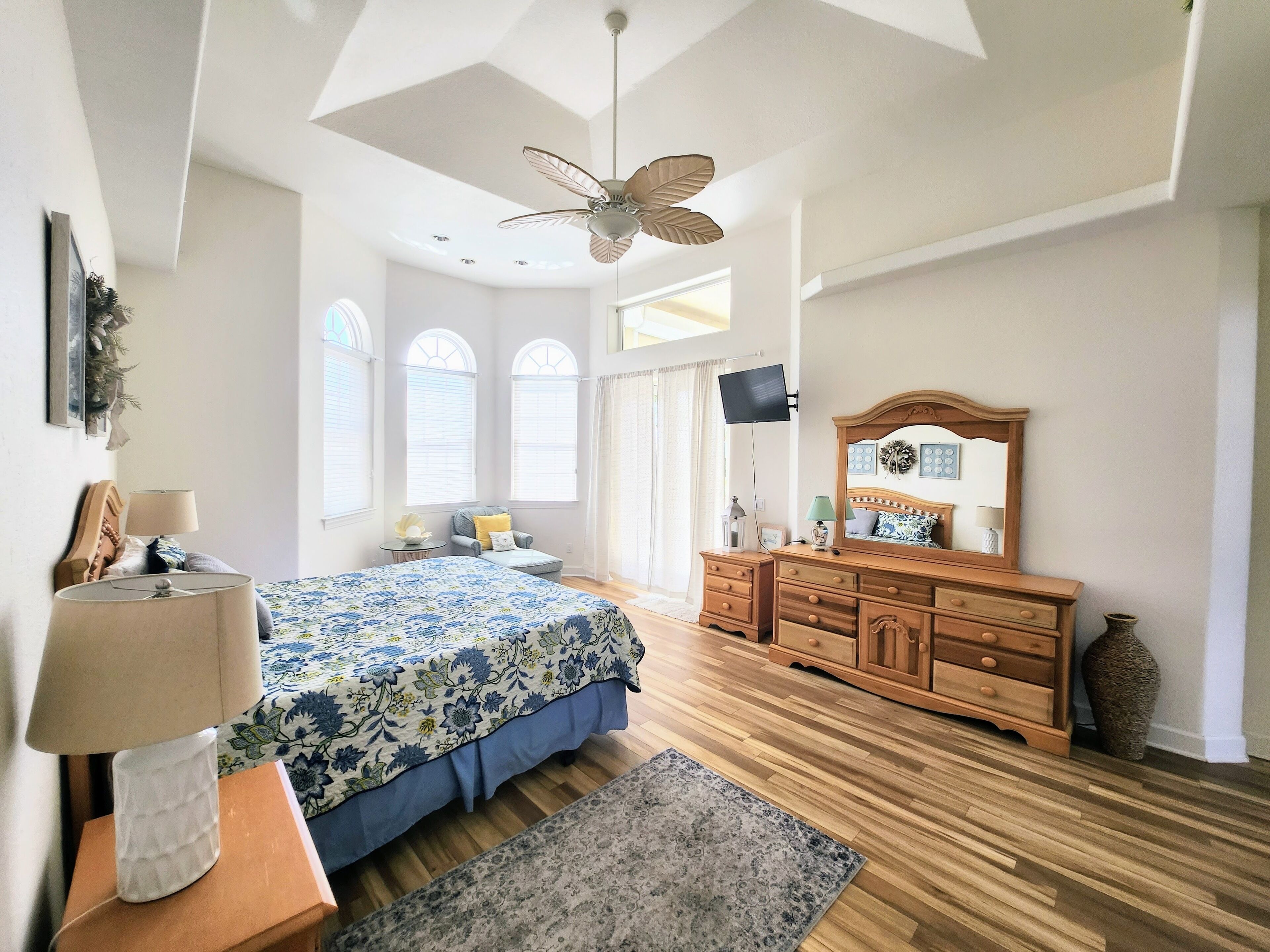 A bedroom with a bed, dresser, vanity, and a ceiling fan.