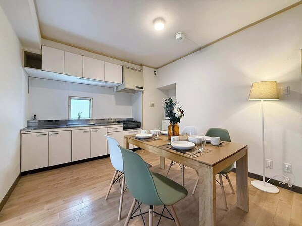 Cocina compacta con armarios blancos, estufa y comedor con mesa y sillas de madera.