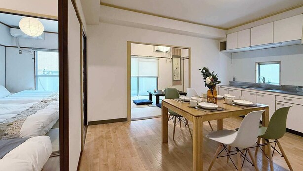 A modern hotel room with a bed, a dining area with a table and chairs, and a kitchen area.