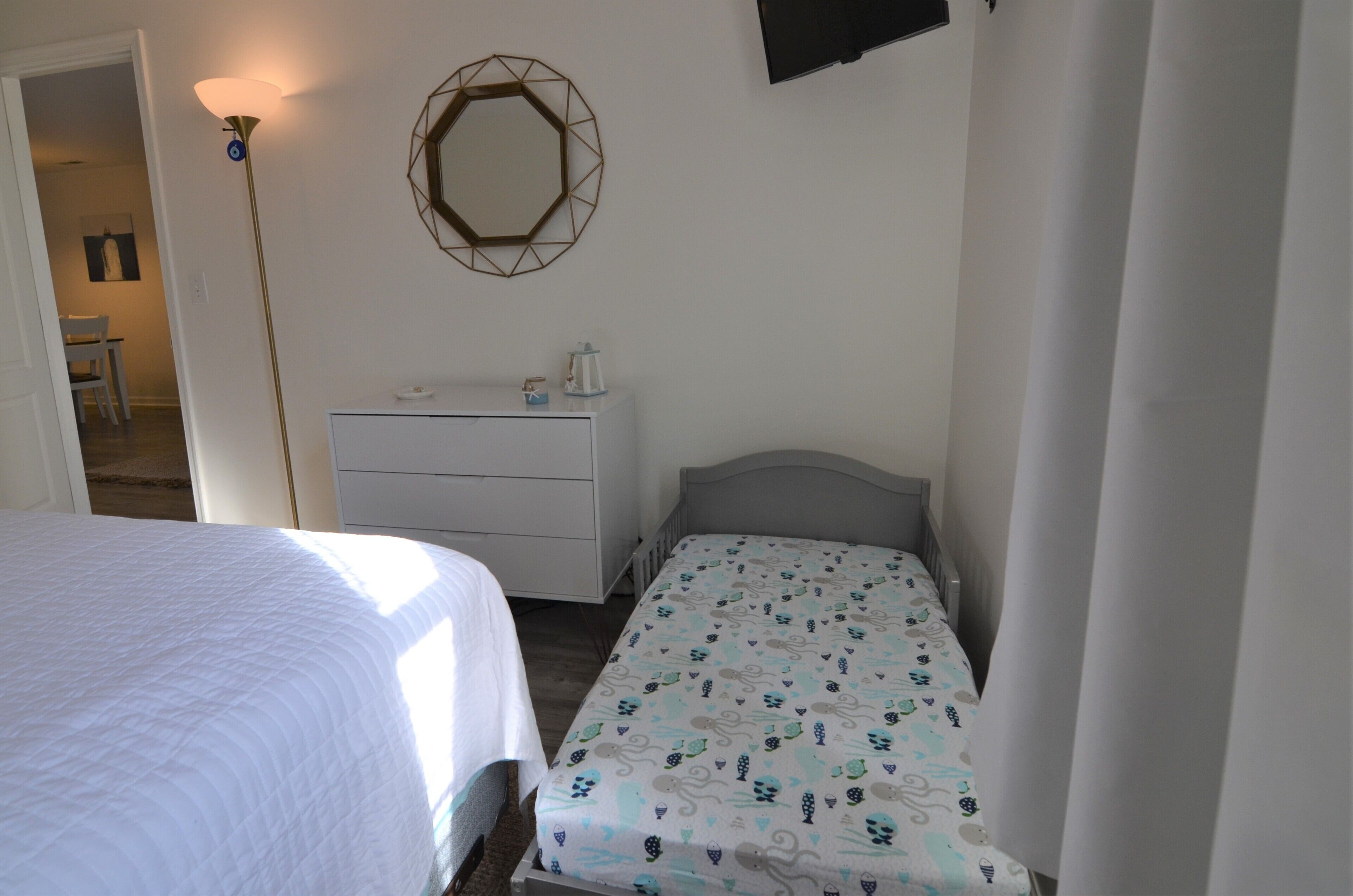 Et soveværelse med seng, natbord, kommode, spejl og lampe.