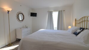 A bedroom with a bed, a dresser, a television on the wall, and a floor lamp.