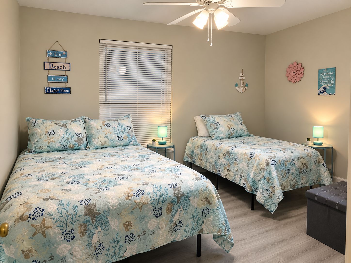 A bedroom with two beds, each with matching floral bedding, a ceiling fan, and wall decorations including a sign and a flower.