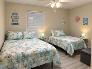 Een slaapkamer met twee bedden, elk voorzien van passend bloemenbeddengoed, een plafondventilator en wanddecoraties, waaronder een bordje en een bloem.