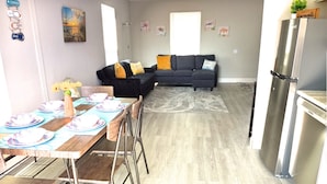 Ein modernes Wohnzimmer mit einer Couch, einem Esstisch gedeckt mit Tellern und einer Küchenzeile mit einem Kühlschrank.