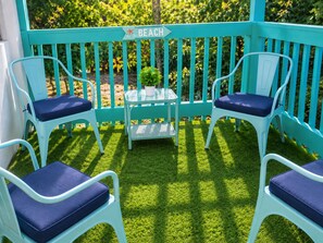A turquoise outdoor seating area with two chairs and a small table, a sign indicating 'Beach', and a potted plant.