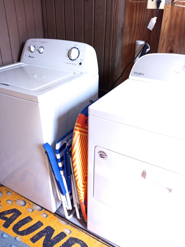 Una lavadora y secadora de carga frontal en un cuarto de lavado con una pared de madera y un tapete amarillo que muestra la palabra "LAUNDRY".