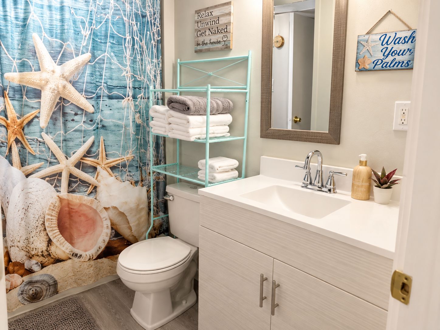 A bathroom with a toilet, sink, and shelves with towels. There are starfish and seashells on the floor.