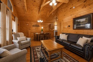 A log cabin interior with a dining area, a leather sofa, and a wooden ceiling.