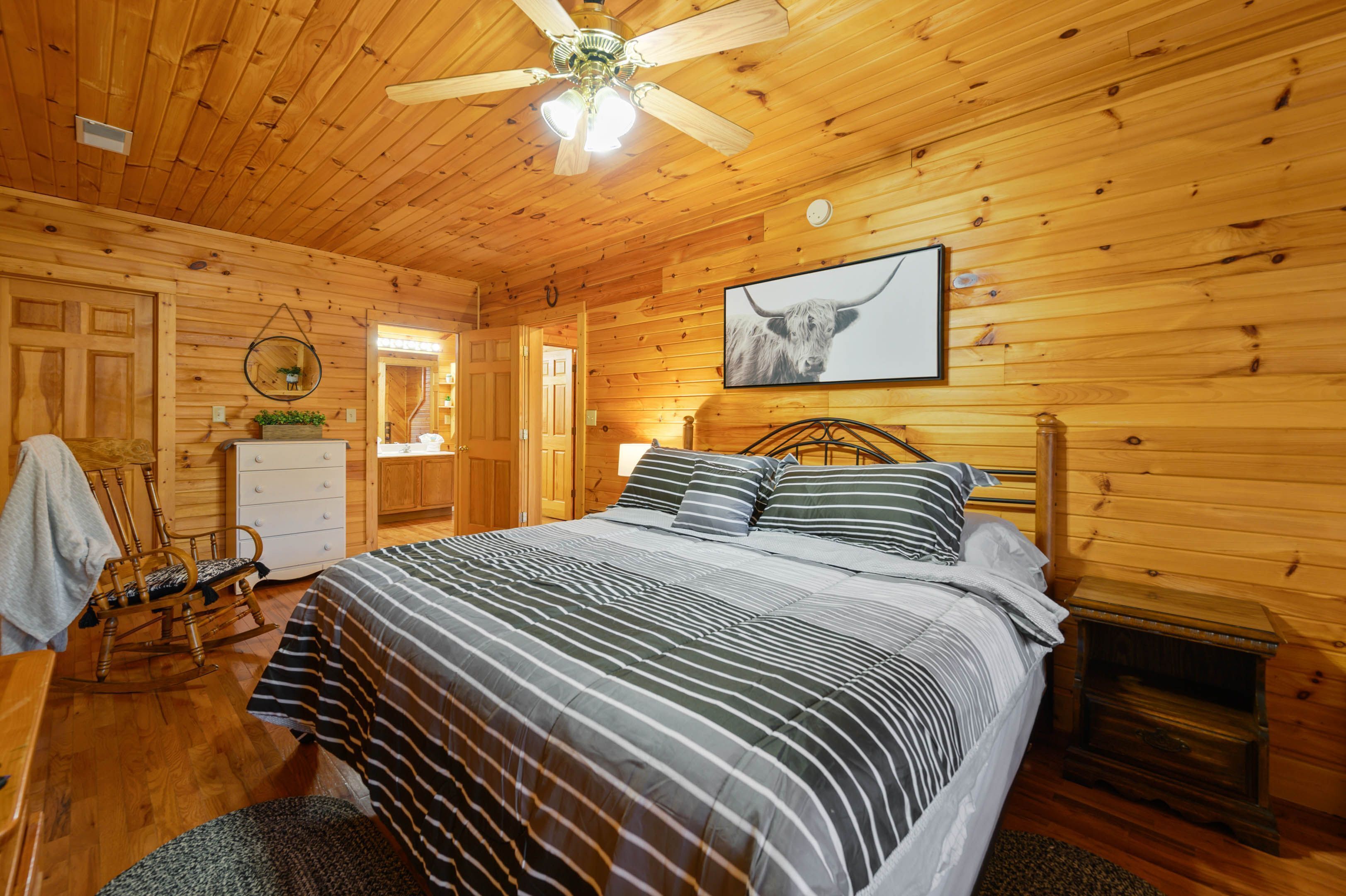 Une chambre à coucher dans une cabane en bois, avec un lit, un fauteuil à bascule, une cheminée et un ventilateur de plafond.