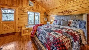 A wooden cabin bedroom with a large bed, a bench by the window, and a rustic decor.