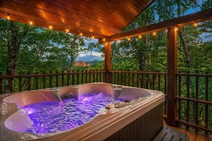 A hot tub with a wooden deck and a view of a town in the background.