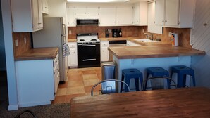 Una cocina con armarios blancos, una estufa, un microondas y taburetes azules.