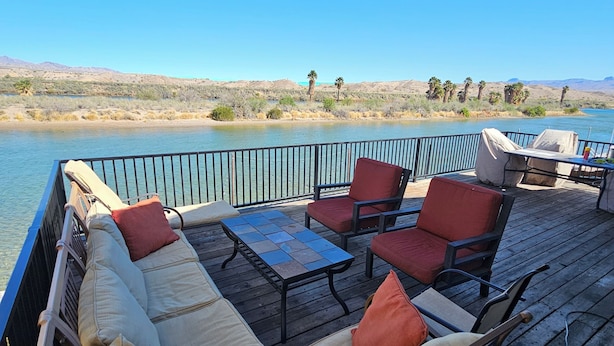 Una terraza con sofá y sillones, con vista a un cuerpo de agua y paisaje desértico.