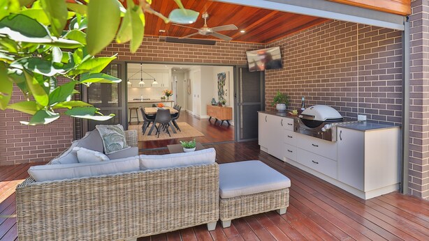 Ein moderner Außenbereich mit Rattan-Sofa, Esstisch und Grillstation.