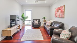Ein modernes Wohnzimmer mit Flachbildfernseher, Ledersofas, einer Holzunterhaltungseinheit und einem großen Fenster.