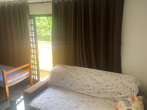 A room with a sofa, a wooden chair, and a window with curtains.