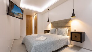 Un dormitorio moderno con una cama grande, televisor montado y lámparas colgantes.
