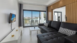 Una sala de estar moderna con un sofá negro, una mesa de centro blanca y un televisor en la pared.