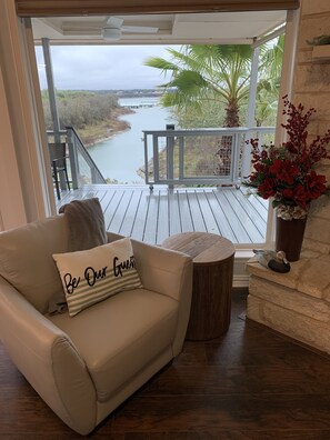 Un salon chaleureux avec un canapé beige, une table ronde en bois et une vue sur une rivière et un pont, visible à travers de grandes fenêtres.